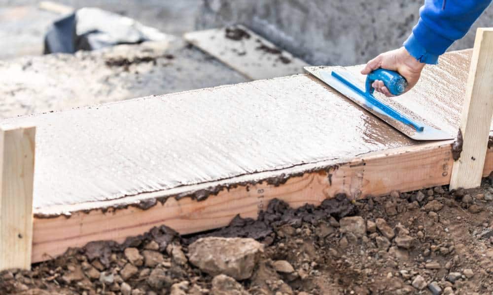 Worker smoothing concrete with trowel at construction site.