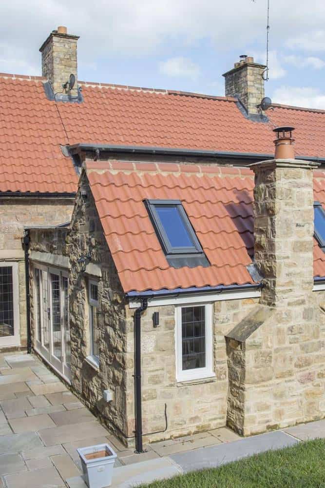 Traditional stone cottage with red-tiled roof and skylights.