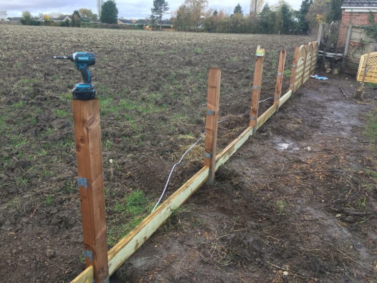 New wooden fence construction in muddy field.