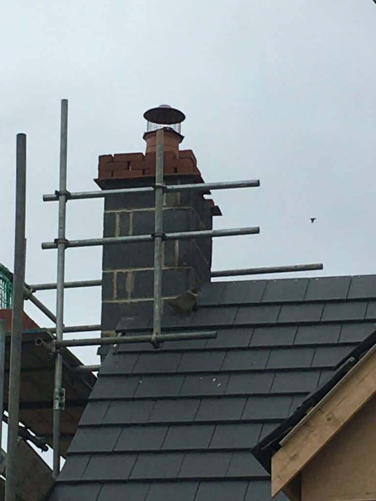 Chimney with cowl on tiled roof, scaffolding.