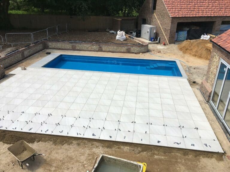 Swimming pool construction with patio tiling in progress.