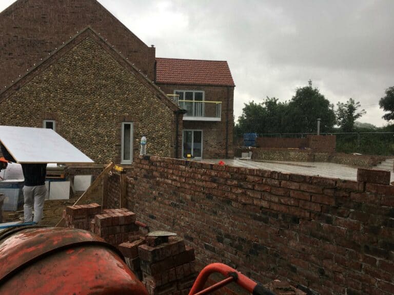 Brick house extension construction under rainy weather.