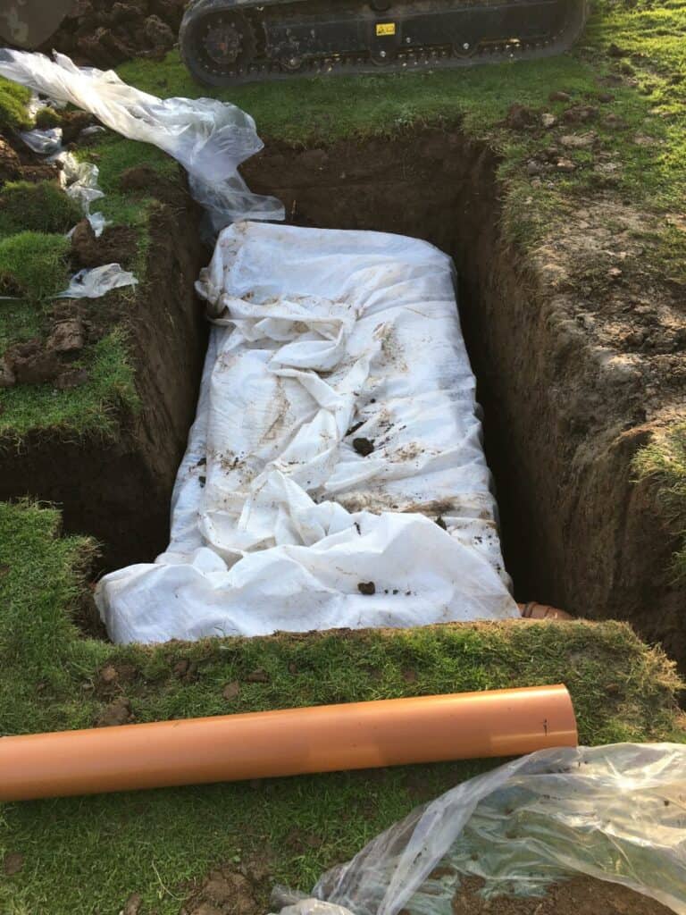 Trench with geotextile and new drainage pipe installation.