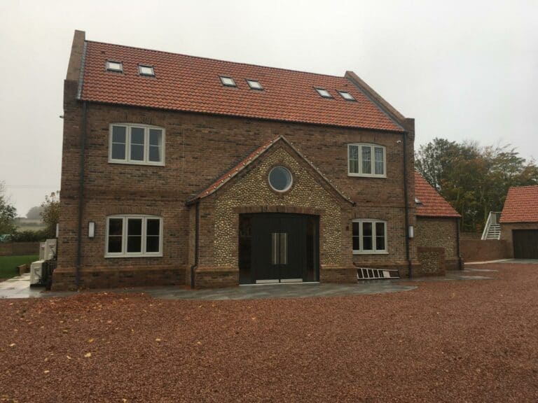 Traditional brick house with gravel driveway in rural setting.