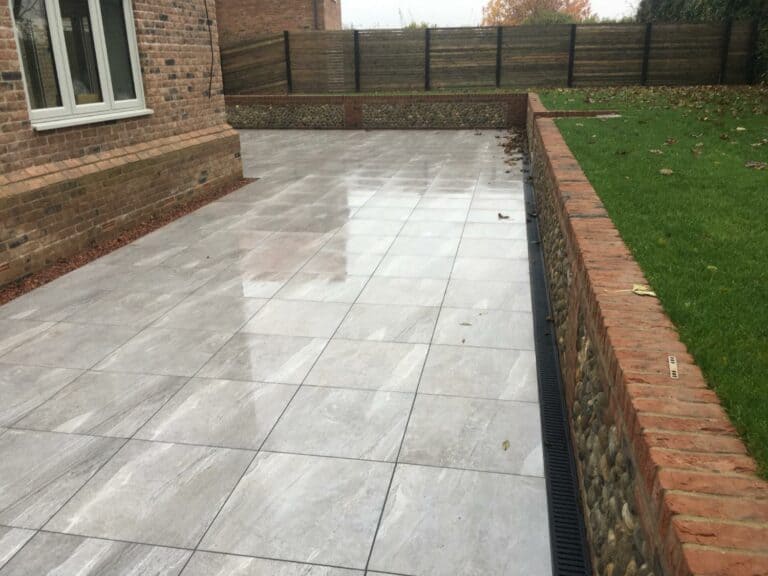 Paved garden patio with wet tiles and lawn.