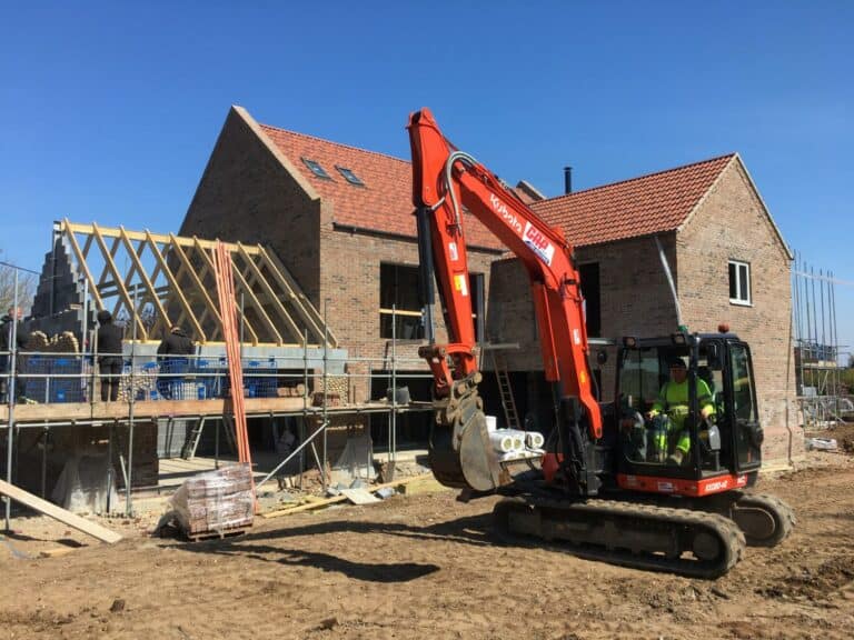 House construction site with excavator and workers.