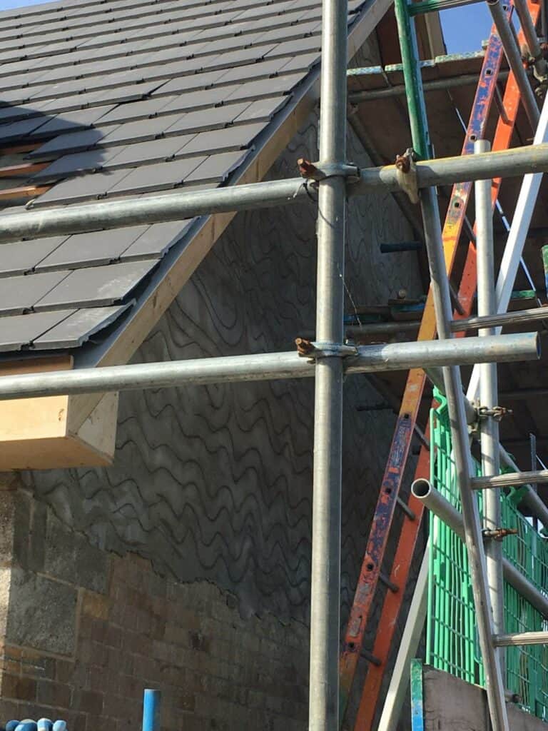 Scaffolding around house with partial roof tile installation.