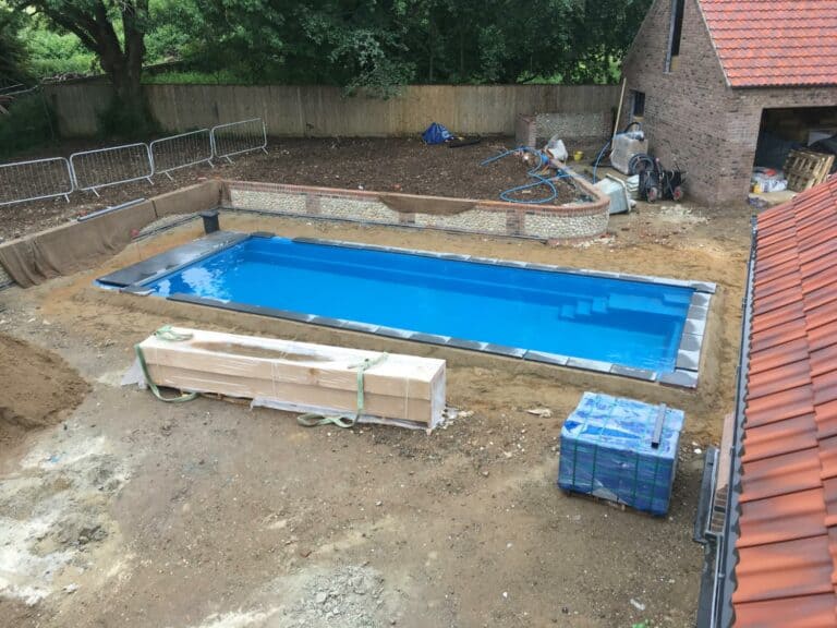 Swimming pool construction in backyard, materials scattered around.