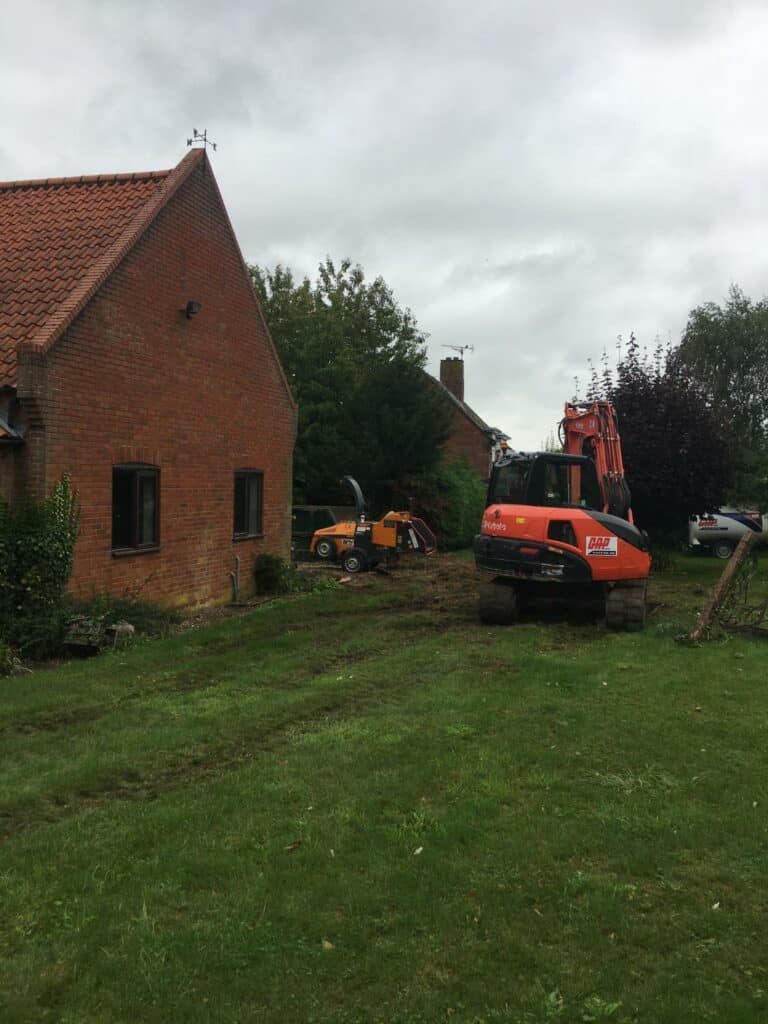 Excavator and dumper conducting garden landscaping near brick house.