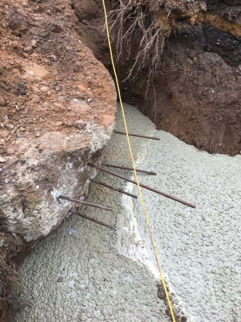 Eroded soil with exposed rebar and measuring tape.