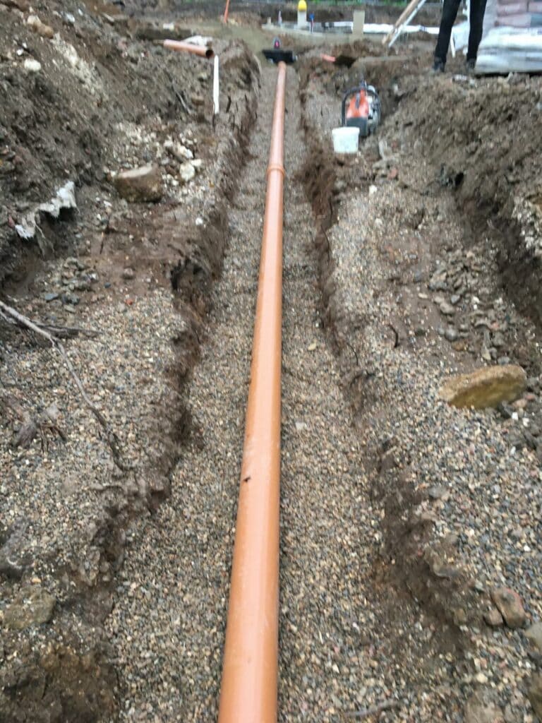 Laying new orange pipeline in trench at construction site.