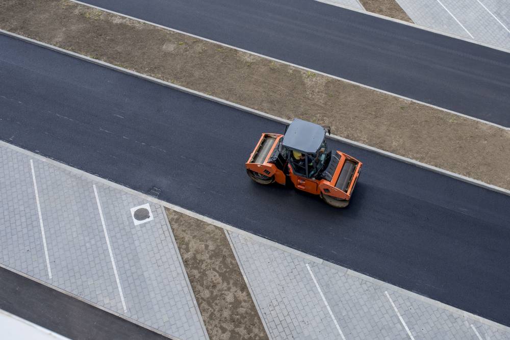 Orange road roller smoothing asphalt.