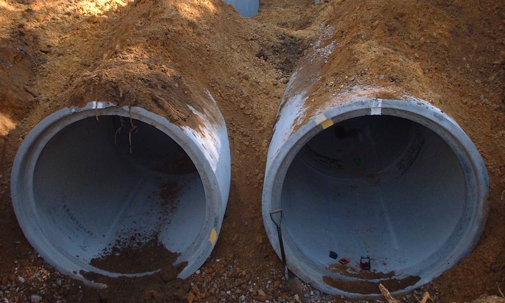 Two large concrete sewage pipes in a trench.